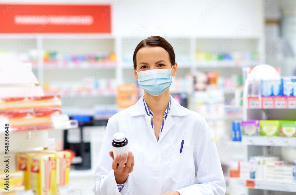 medicine, pharmaceutics and healthcare concept - happy female apothecary wearing face protective medical mask for protection from virus disease with drug at pharmacy