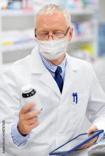 medicine, healthcare and technology concept - senior apothecary wearing face protective medical mask for protection from virus disease with tablet pc computer at pharmacy