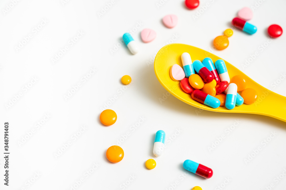 A lot of pills colorful in yellow plastic spoon on the white background. Medicine pills, tablets and capsules with copy space for text. A lot of pills colorful in yellow plastic spoon on the white background. Medicine pills, tablets and capsules with copy space for text.