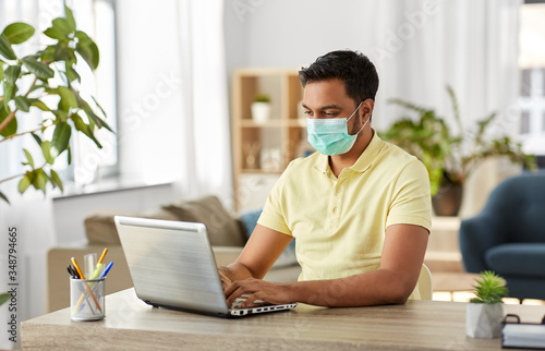 quarantine, remote job and pandemic concept - indian man wearing face protective medical mask for protection from virus disease with laptop computer working at home office