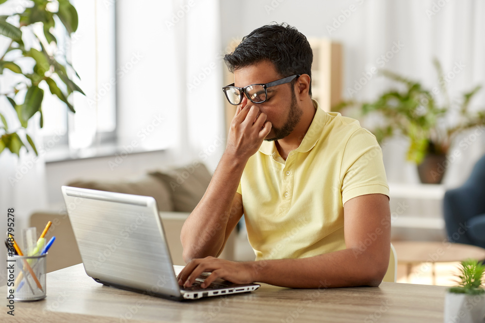 remote job, technology and people concept - tired young indian man in glasses with laptop computer working and rubbing his nose bridge at home office remote job, technology and people concept - tired young indian man in glasses with laptop computer working and rubbing his nose bridge at home office