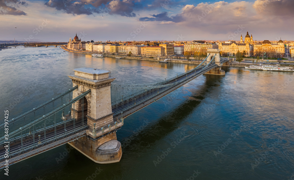 Budapest, Hungary - Aerial panoramic view of the famous Szechenyi Chain Bridge at sunset with Parliament building, sightseeing boats, St.Stephen's Basilica and nice colorful clouds at background