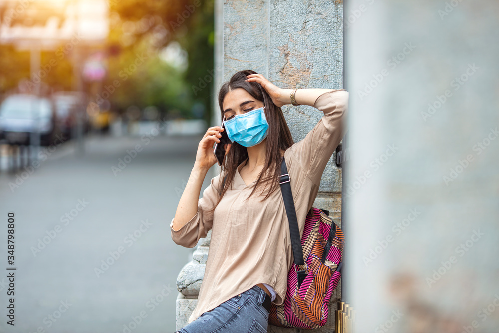 Woman wearing a face mask walking outdoors and using cell phone. Portrait of young woman on the street wearing face protective mask to prevent Coronavirus and anti-smog and using smartphone
