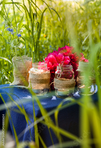 picnic table on the grass background. The table is decorated with jars in a rustic style and peonies