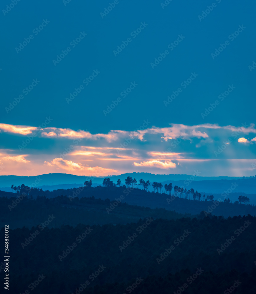 Different layers of hills at sunset with cloudy blue sky