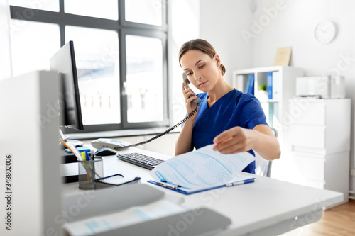 medicine, technology and healthcare concept - female doctor or nurse with computer and clipboard calling on phone at hospital