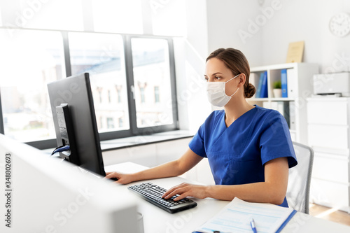 medicine, technology and healthcare concept - female doctor or nurse wearing face protective medical mask for protection from virus disease with computer working at hospital