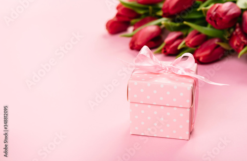 Gift box with a pink ribbon in white polka dots on a background of a bouquet of red tulips with free space for text. Wallpaper or banner for gift shop, flower shop or jewelry store. © Hanna