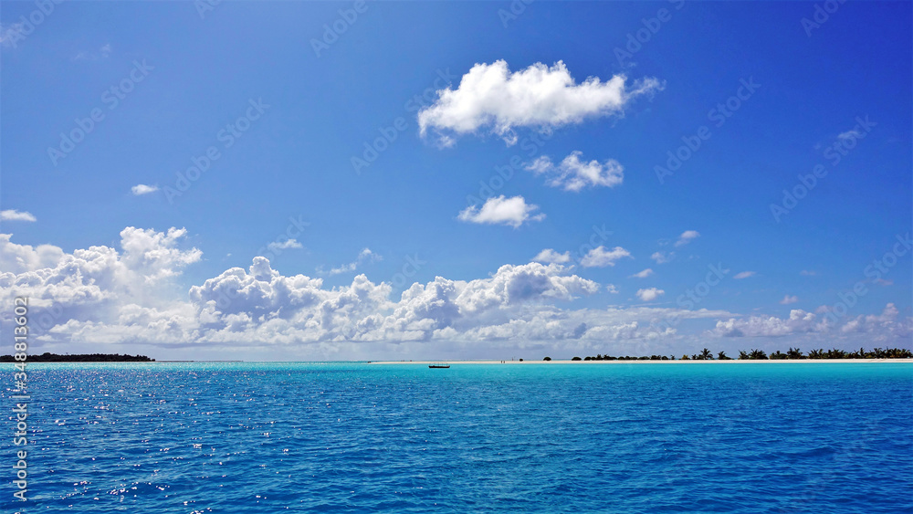 Amazing colors of the Indian Ocean. Maldives. Water colors of turquoise and aquamarine, blue sky with beautiful clouds. In the distance is a boat, a sandy beach with palm outlines. Paradise.