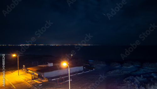 Night scene on the beach. With street lamps and city lights across the sea on the horizon. Top view. Pomorie resort, Bulgaria.