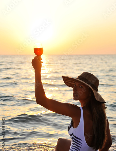  Summer time. Woman in big hat with glasswine on sunset beach.