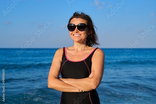 Portrait of beautiful mature woman in sunglasses swimsuit smiling looking at camera