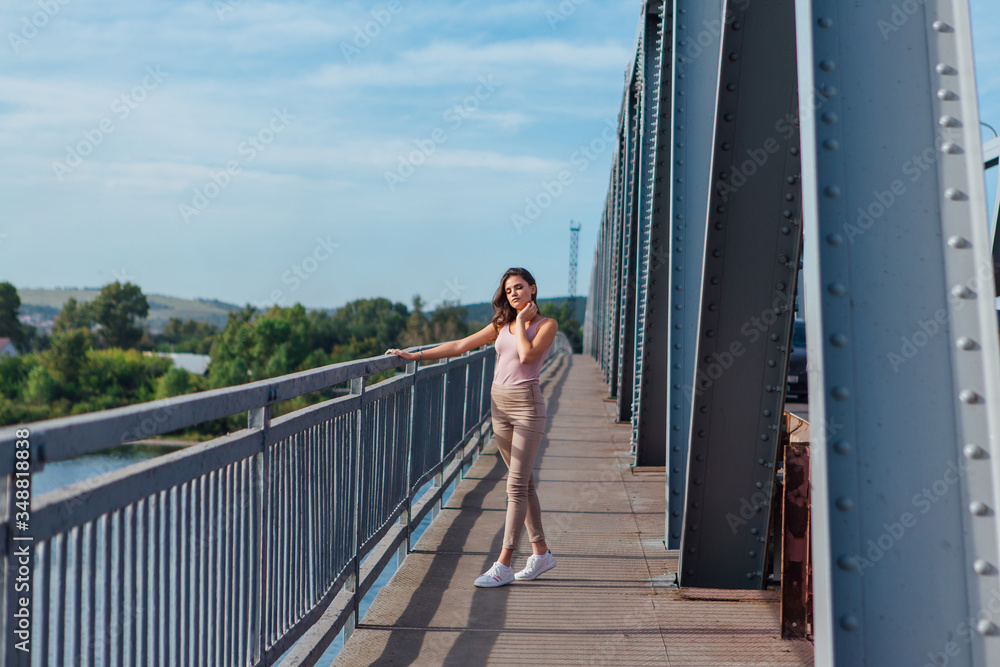 Pretty young woman posing on the old rusty transport bridge over the river during sunset.