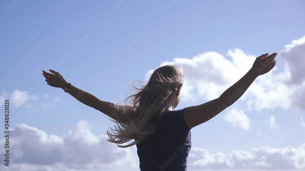 Back view of young caucasian girl with raised hands towards a blue sky on a sunny day. Close-up Back view of young caucasian girl with raised hands towards a blue sky on a sunny day. Close-up