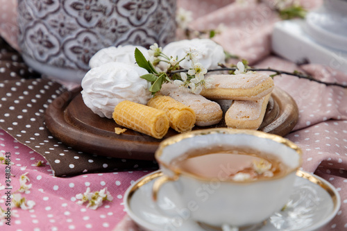 White porcelain tea cup with flowers on a white saucer and sweets on a summer table