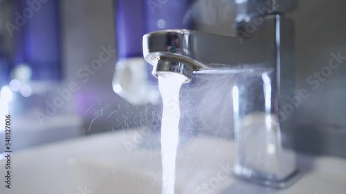 Steam from hot water in the sink. Hot tap water. Warm water flows from the tap in the bathroom. Prevention of a coronavirus pandemic by washing hands with soap. Water jet. Hand hygiene.