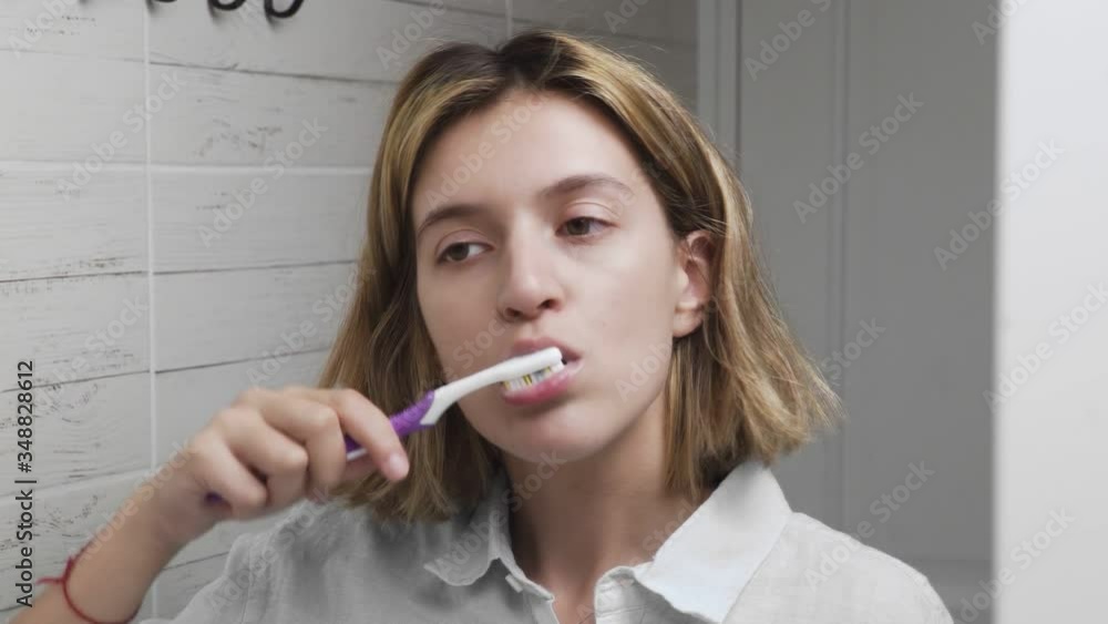 Young beautiful girl with toothbrush. Brushing teeth. Closeup of woman brushing her teeth and looking at the mirror Young beautiful girl with toothbrush. Brushing teeth. Closeup of woman brushing her teeth and looking at the mirror