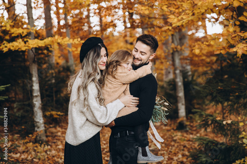 Stylish family in the autumn forest. Models. A young guy and a girl stand on a forest road among yellow leaves and hold their daughter in their arms.
