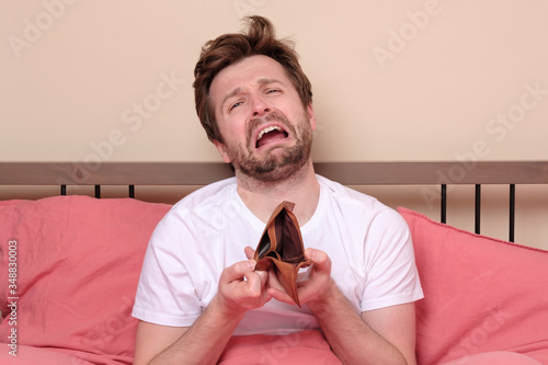 Stressed man being confused about his empty wallet sitting at bed in quarantine.