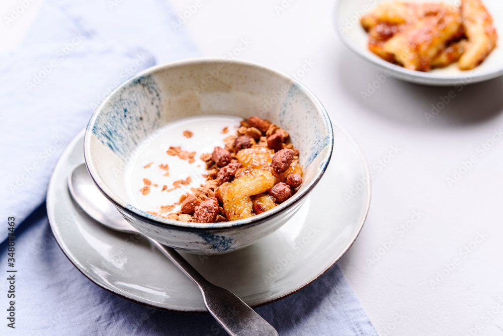 Healthy breakfast yogurt bowl with granola and caramelized bananas and nuts on grey concrete background. Selective focus Healthy breakfast yogurt bowl with granola and caramelized bananas and nuts on grey concrete background. Selective focus