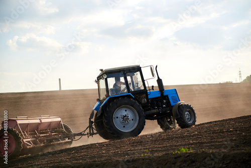 Fototapeta Naklejka Na Ścianę i Meble -  Agricultural work on field with black soil. Blue tractor riding and seeding countryside. Rural works in spring. Environmental protection concept. Ecological products cultivation. Natural background.