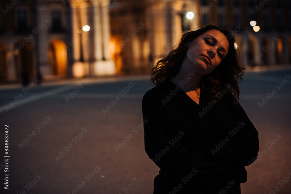 Half length portrait of young woman wearing black, standing alone in the street with contemplative face expression. Night time, street light. Safety concept, night life or loneliness concept Half length portrait of young woman wearing black, standing alone in the street with contemplative face expression. Night time, street light. Safety concept, night life or loneliness concept