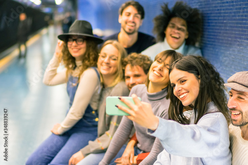 Group of friends using mobile phone in metro subway for a selfies. Smiling people waiting of the next train and playing with the cellular phone. Concept of people addicted to technology trends - Image