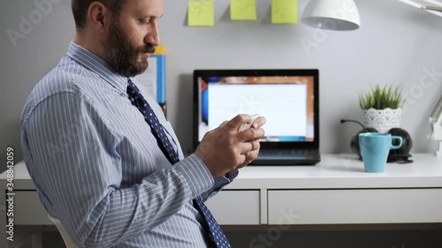 Office worker loafer is playing on phone. Bearded man sitting at workplace in office takes off from work and plays video games on mobile phone photo