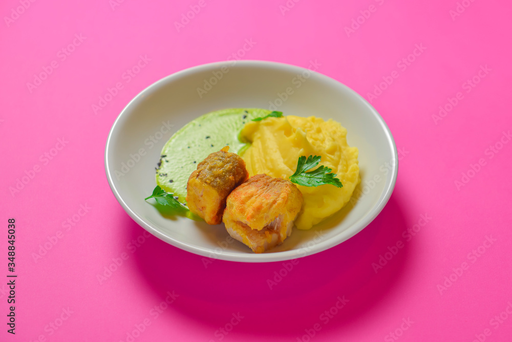 Grilled fried fish with mashed potato and sauce served in a white plate isolated on bright pink background.