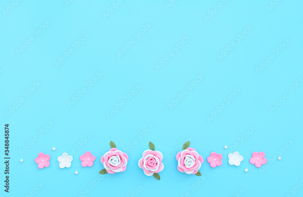 Pink and white flowers made of foamiran with green leaves and white beads on blue background. Mother day, Valentine day, Wedding, Birthday concept. Greeting or invitation card. Flat lay, copy space.