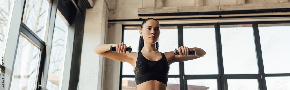 Panoramic shot of sportswoman training with dumbbells in gym - obrazy, fototapety, plakaty 