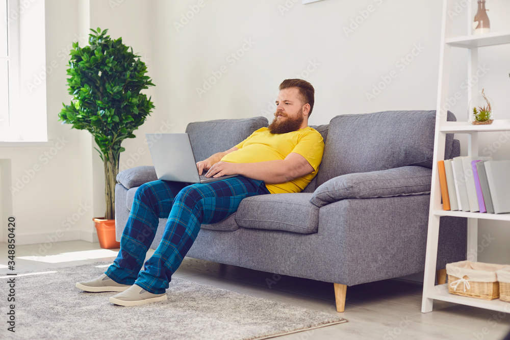 Online job working communication date. Funny man with a beard is typing in a laptop sitting on sofa home
