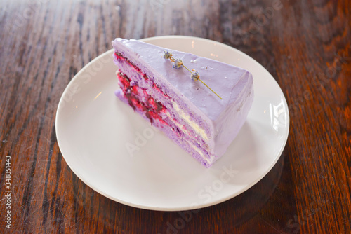 Slice of purple lavender cake with berries served with lavender flowers on a white plate.