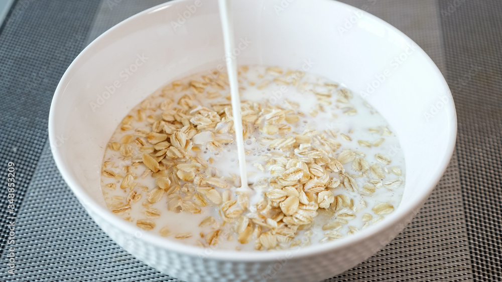 person pours fresh milk into ceramic bowl with tasty porridge cereals on grey table in hotel restaurant extreme close view person pours fresh milk into ceramic bowl with tasty porridge cereals on grey table in hotel restaurant extreme close view