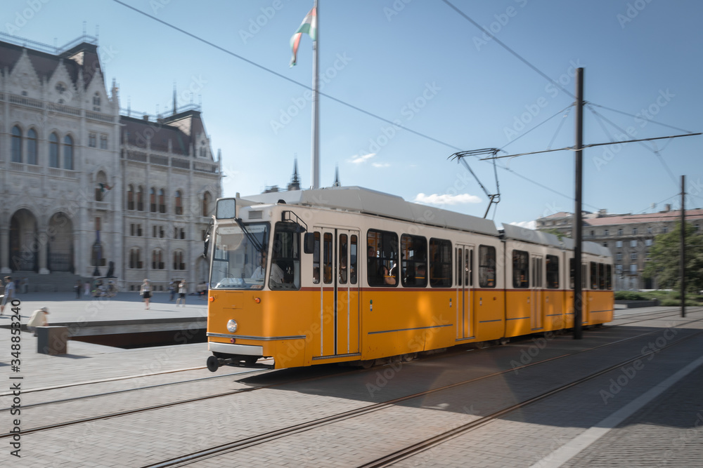 Yellow tram rides in the city. Photo of a tram in motion on a blurred background.