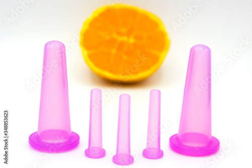 five different sized anti cellulite pink cosmetic vacuum jars for body and face with orange on white background. Close up. Home spa treatments. photo