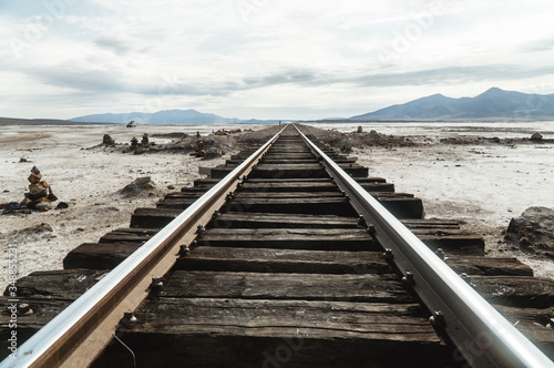 Wooden Train Track Railway lines. Bolivia Salt Flats mountain landscape. Bolivian salty desert and blue sky background. Train Cemetery, Salar de Uyuni. Symmetry, transport, travel, tourism, journey