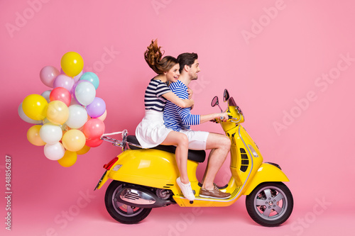 Profile side view portrait of his he her she nice attractive cheerful cheery couple riding moped carrying bringing delivering air balls having fun weekend isolated on pink pastel color background