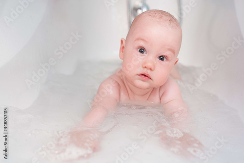 Adorable bath boy. Newborn baby bathing. Home swimming lessons. Little child in a bathtub. Smiling kid in bathroom. Infant washing and bathing. Hygiene and care for young children.