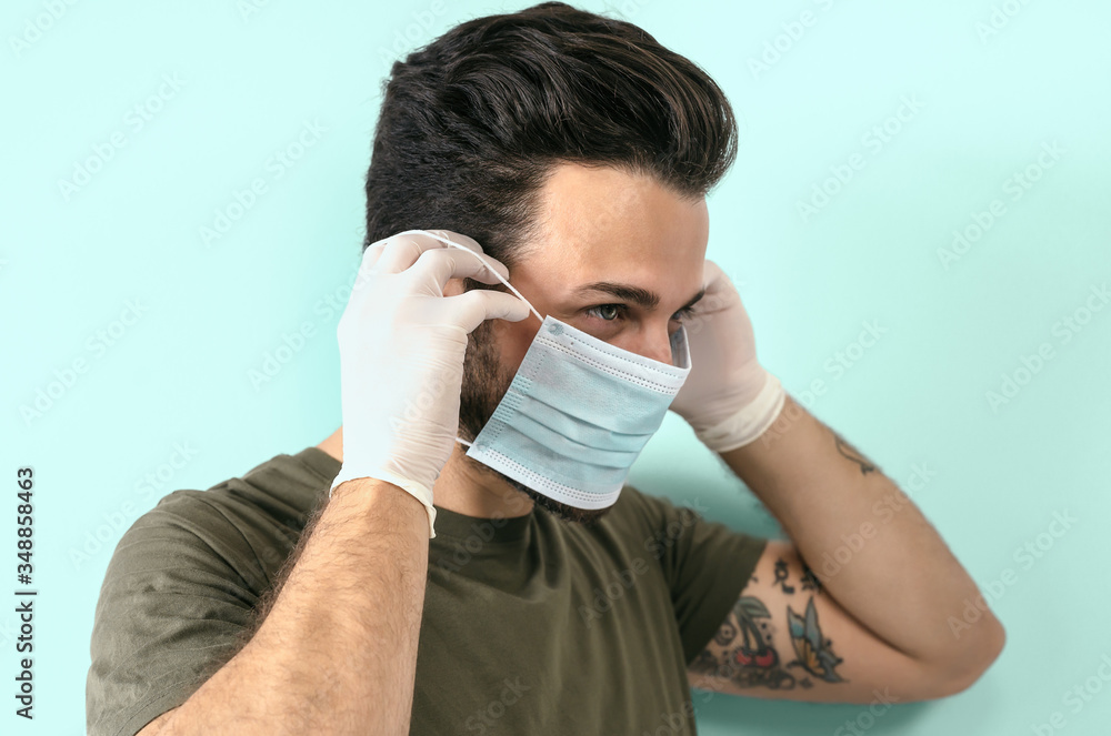 Young man portrait wearing surgical face mask and gloves - People self quarantine for preventing and stop corona virus spreading - Healthcare and coronavirus spread concept - Aquamarine background Young man portrait wearing surgical face mask and gloves - People self quarantine for preventing and stop corona virus spreading - Healthcare and coronavirus spread concept - Aquamarine background