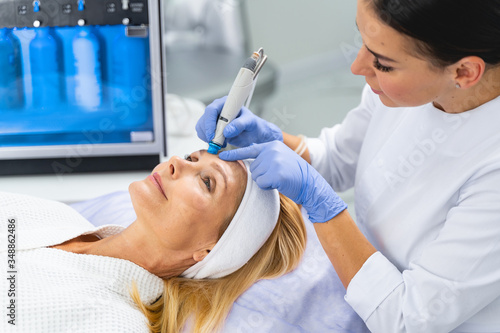 Professional female cosmetologist performing a microdermabrasion treatment photo