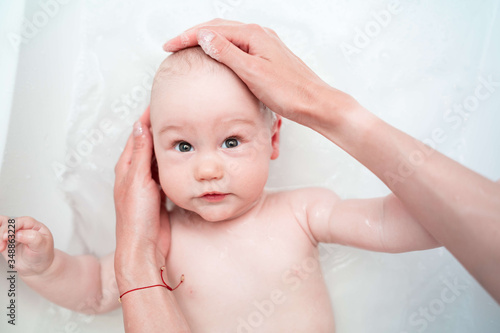 Mother's hands washing a baby. A baby boy bathes in a bath. Caring mother's hands. Happy infant while taking a bath. Hygiene and care for young children. Top view.