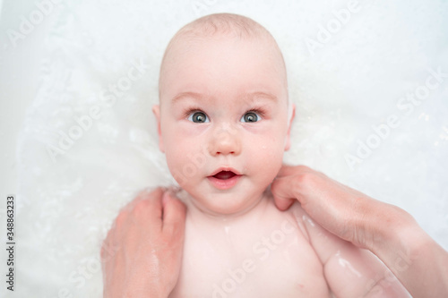 Adorable bath boy. Newborn baby bathing. Caring mother's hands. Hygiene and care for young children. Top view.