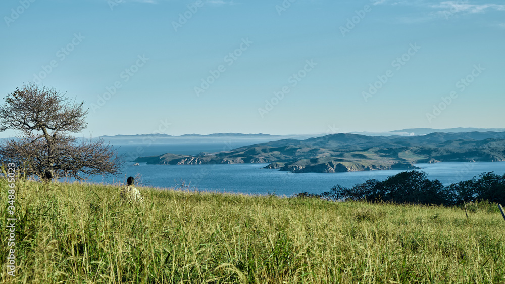 girl climbing to the top of the hill over the fresh green grass in the morning with sea and mountains background. Adventure and outdoor concept.