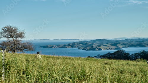 girl climbing to the top of the hill over the fresh green grass in the morning with sea and mountains background. Adventure and outdoor concept.