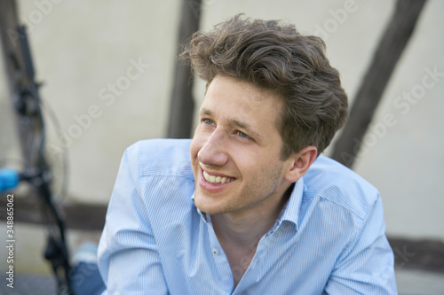 Portrait of a young handsome man with brown curls and a three-day beard, sitting there in a blue stylish shirt, smiling with white teeth