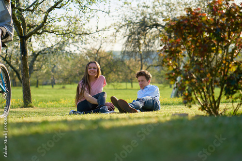 Young couple making a break in the country in Germany, laying on the ground on a meadow, looking after a cyclist, you can see trees and bushes