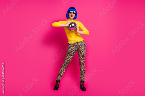 Full length photo of funny club lady youth costume theme party hold disco ball wear specs yellow turtleneck blue short wig shoes leopard pants isolated vibrant pink color background
