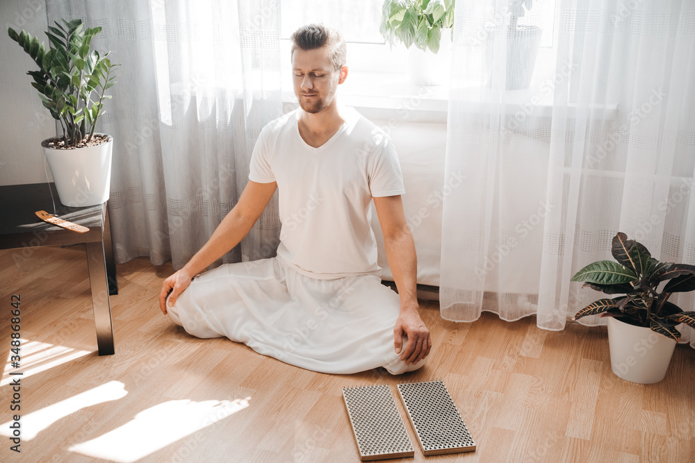 Young man meditating on his living room on the floor, sitting in the lotus position with closed eyes. Expression of tranquility in a health, mindfulness and fitness concept. Young man meditating on his living room on the floor, sitting in the lotus position with closed eyes. Expression of tranquility in a health, mindfulness and fitness concept.