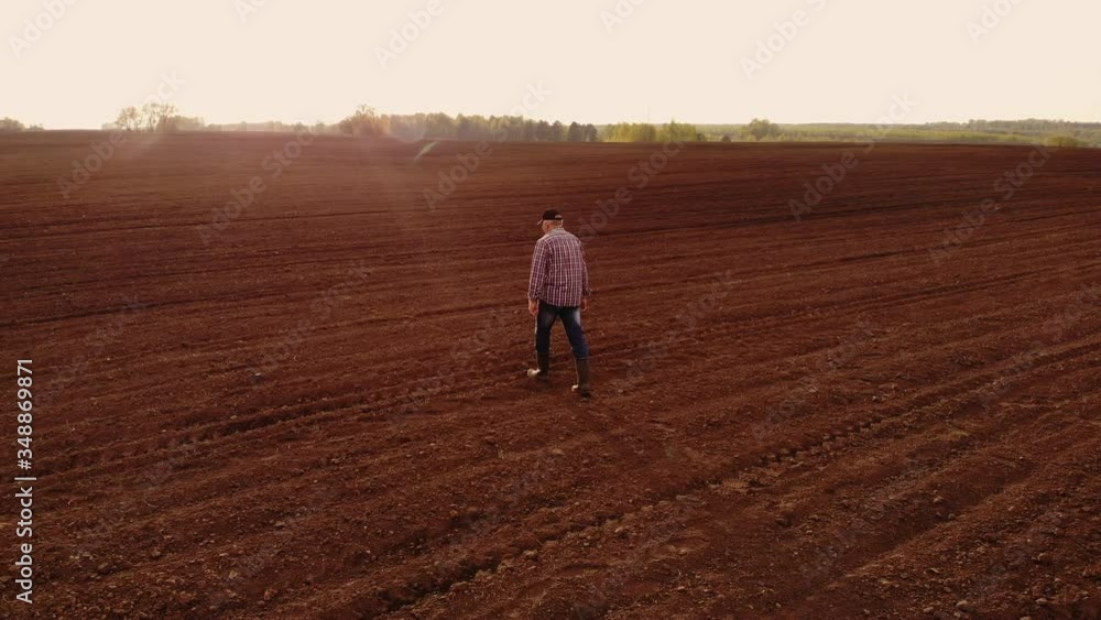 Aerial view of farmer walking through his fields. An adult male farmer in a cap walks across a plowed field and with planted crops in his boots. Top view of a man inspecting the fields. Farmer. Aerial view of farmer walking through his fields. An adult male farmer in a cap walks across a plowed field and with planted crops in his boots. Top view of a man inspecting the fields. Farmer.